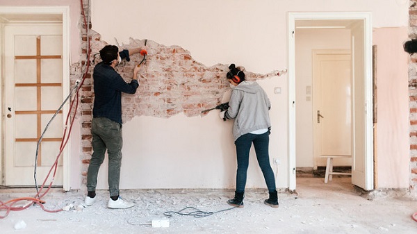A couple scraping off the paint from a wall in their home
