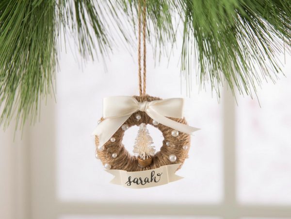 A mini holiday wreath ornament hanging from a chirstmas tree