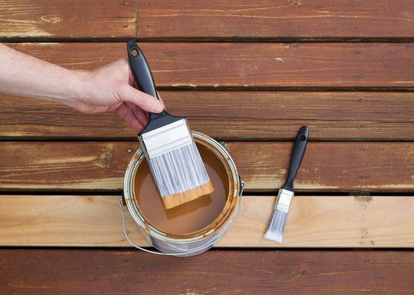 A person painting the wooden deck with a paint brush