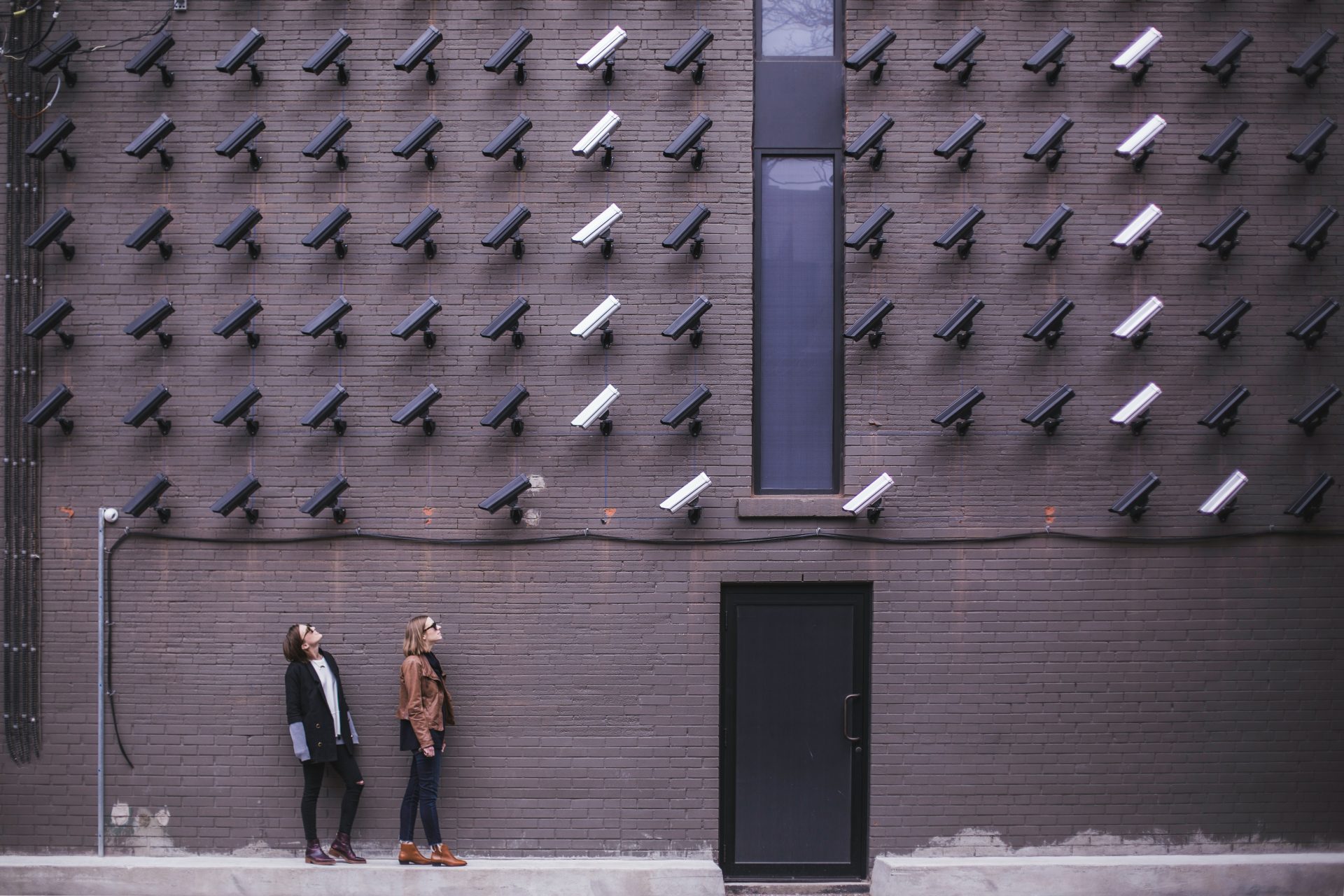 two people looking up at a wall covered in security cameras to illustrate that self storage is more safe than keeping possessions at home
