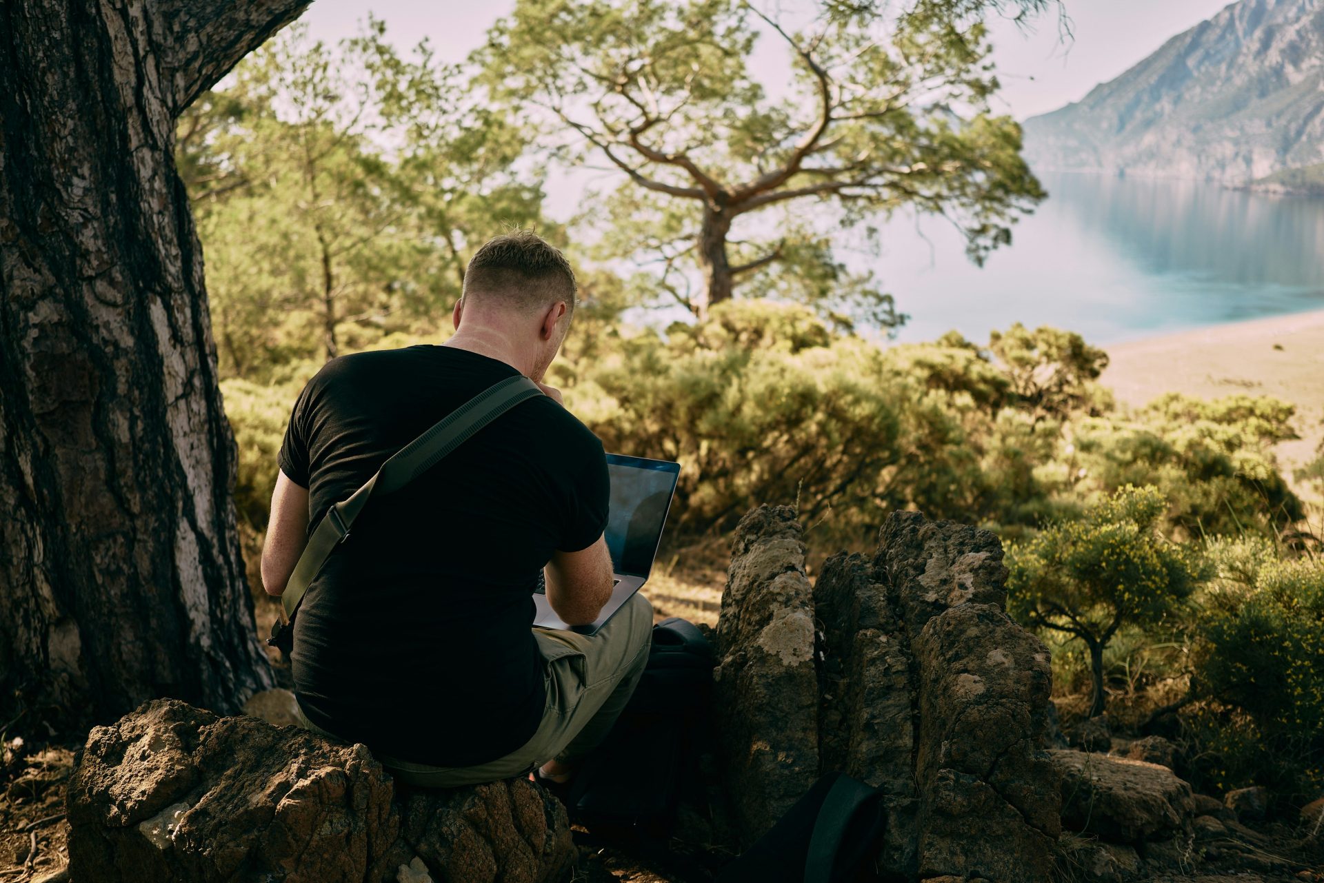 man working on his laptop in the bush overlooking the beach